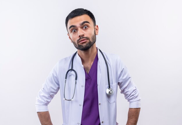 Surpris jeune médecin de sexe masculin portant une robe médicale stéthoscope sur blanc isolé