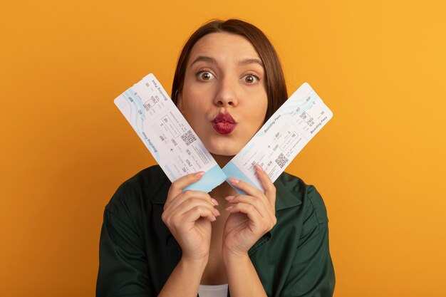Surpris jolie femme détient des billets d'avion près du visage isolé sur mur orange