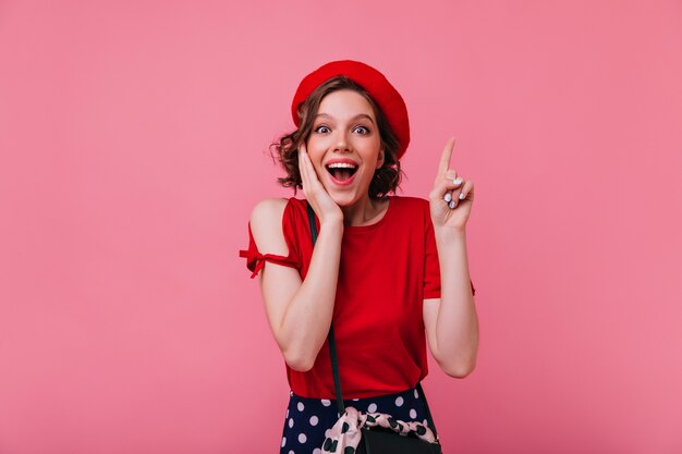 Surpris jolie fille avec tatouage exprimant des émotions positives. dame française raffinée en béret et t-shirt rouge.