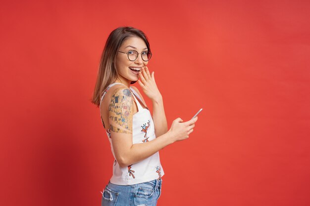 Surpris jolie fille avec un téléphone dans les mains sur le mur rouge