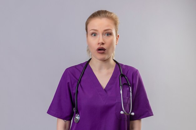 Surpris médecin jeune fille portant une robe médicale violette et un stéthoscope sur fond blanc isolé