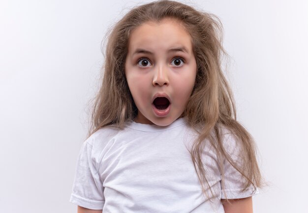 Surpris petite écolière portant un t-shirt blanc bouche ouverte sur fond blanc isolé