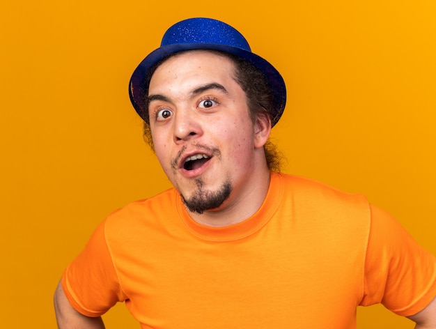 Surpris à la recherche d'un jeune homme portant un chapeau de fête isolé sur un mur orange