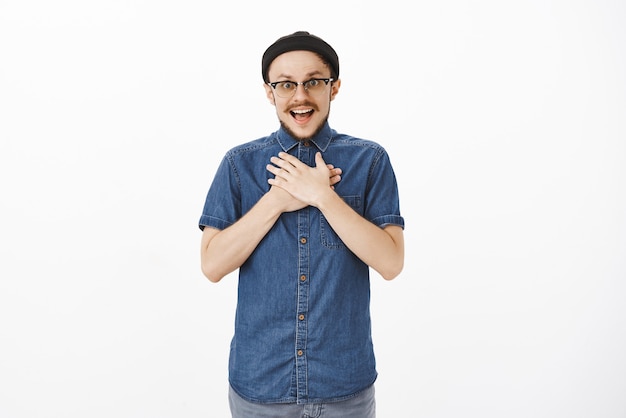 surpris et reconnaissant beau collègue masculin félicité avec b-day par l'équipe se tenant la main sur la poitrine et haletant d'étonnement et de plaisir remerciant sur un mur blanc