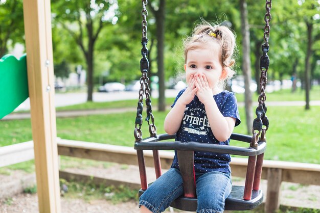 Surprise mignonne petite fille assise sur la balançoire