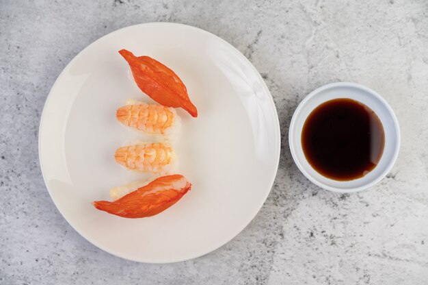 Le sushi est sur une assiette avec une trempette sur un sol en ciment blanc.