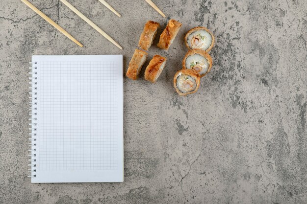 Sushi frit avec des baguettes et un cahier sur un fond de pierre.