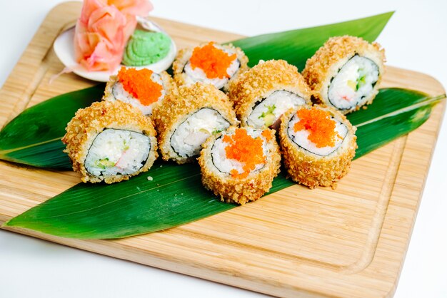 Sushis chauds avec des bâtons de crabe, avocat servi sur des feuilles de bois