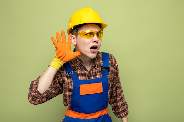 Photo gratuite suspect montrant le geste d'écoute jeune constructeur masculin portant l'uniforme et des gants avec des lunettes