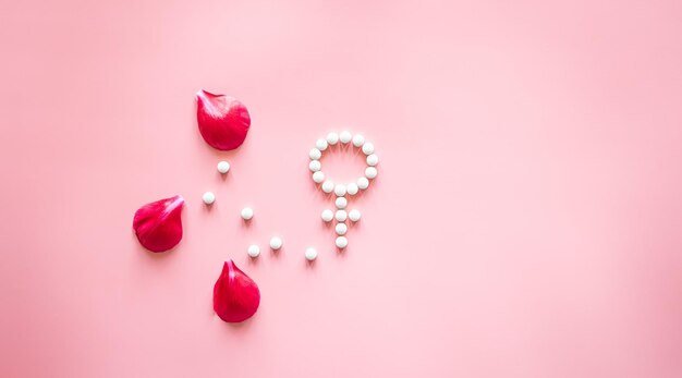 Symbole de genre vénus composé de pilules et de pétales de fleurs de pivoine sur fond rose
