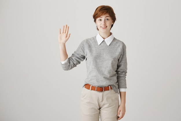 Photo gratuite sympathique fille rousse souriante avec coupe de cheveux courte posant contre le mur blanc