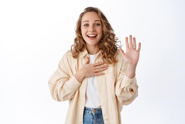 Sympathique jeune femme levant la main et touchant le nom de la poitrine elle-même fait une introduction disant la vérité sincère et souriant debout sur fond blanc