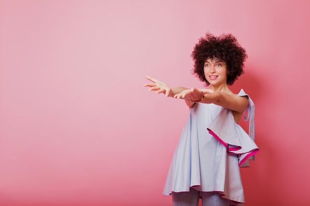 Sympathique jolie femme aux cheveux courts foncés chemise bleue habillée tire ses mains et pointe sur rose