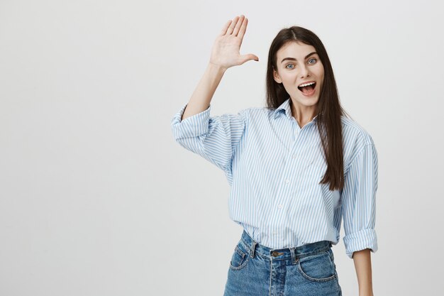 Sympathique jolie femme heureuse en agitant la main levée en bonjour, geste de salutation