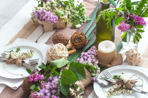 Table décorée magnifiquement élégante pour des vacances avec des fleurs de printemps et des verts - mariage ou Saint Valentin avec des couverts modernes, un arc, un verre, une bougie et un cadeau, horizontal, gros plan, tonique