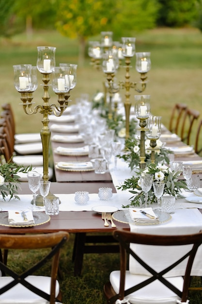 Table de fête de mariage décorée sur l'herbe avec des sièges invités à l'extérieur dans les jardins avec des bougies allumées