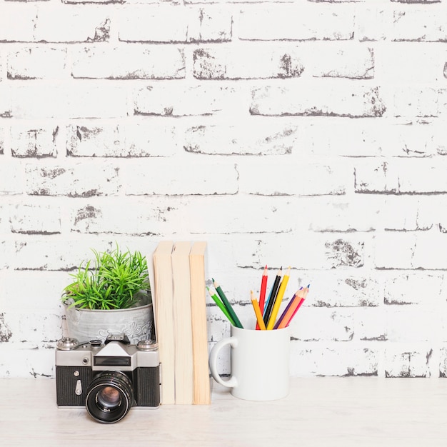 Photo gratuite table avec des livres caméra et des stylos près du mur