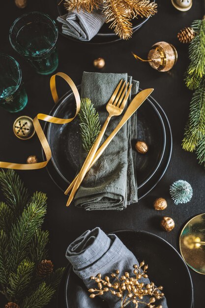 Table de Noël servie dans des tons sombres avec une déco dorée.