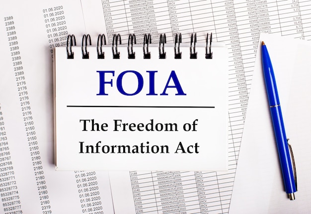 Sur la table se trouvent des graphiques et des rapports sur lesquels se trouvent un stylo bleu et un cahier avec le mot foia the freedom of information act
