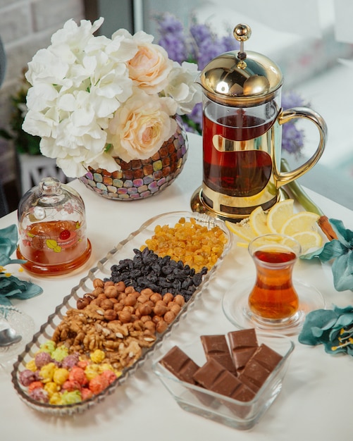 Table à thé avec bouilloire, verre de thé, noix et bonbons.