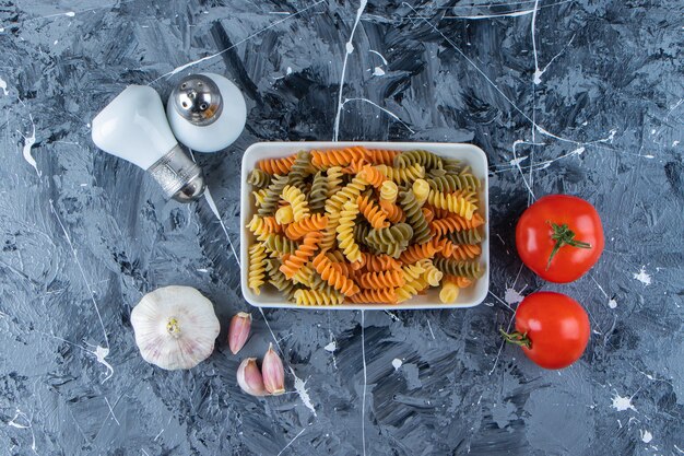 Un tableau blanc de macaronis multicolores avec des tomates rouges fraîches et de l'ail sur une surface en marbre .