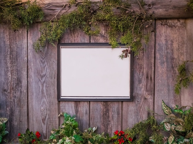 Tableau blanc vide sur une clôture en bois entourée de plantes et de fleurs