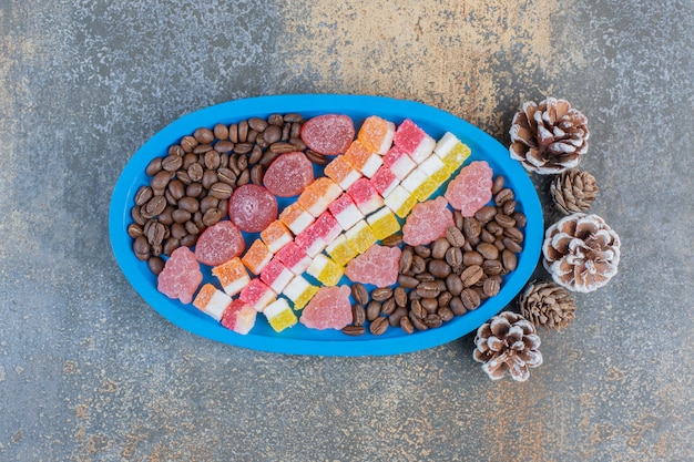 Un tableau bleu plein de différents bonbons à la gelée de fruits avec des pommes de pin. Photo de haute qualité