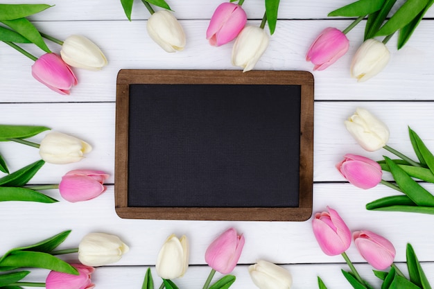 Tableau noir vide avec une composition de printemps avec des tulipes sur bois blanc