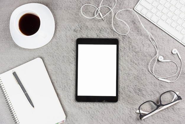 Tablette numérique avec écran blanc entouré de fournitures de bureau et tasse à café sur fond gris