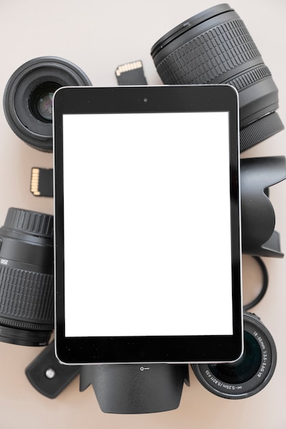 Photo gratuite tablette numérique avec écran blanc sur l'objectif de la caméra et accessoires sur fond coloré