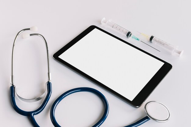 Tablette numérique avec écran vide; seringue et stéthoscope sur fond blanc