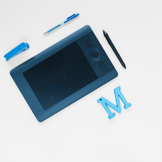 Tablette numérique graphique; stylo; agrafeuse et m alphabet sur la surface blanche