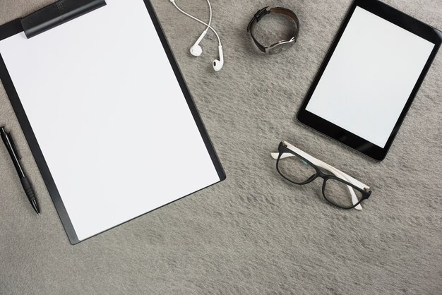 Tablette numérique; presse-papiers; écouteur; montre-bracelet; lunettes et stylo sur fond gris