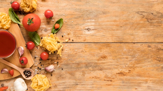 Tagliatelles crues près de ses ingrédients et sa sauce tomate sur un fond en bois texturé