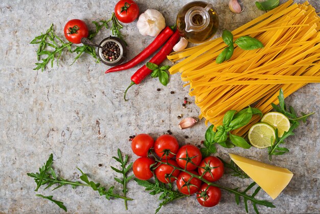 Tagliatelles de pâtes et ingrédients pour la cuisson (tomates, ail, basilic, piment). Vue de dessus