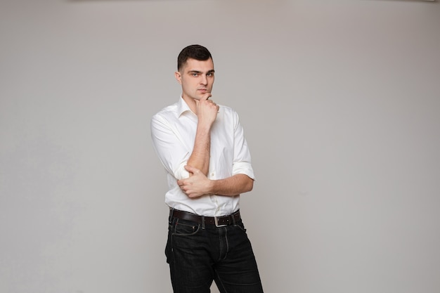 Taille du beau jeune homme en chemise blanche tenant les mains dans les poches tout en posant sur fond noir