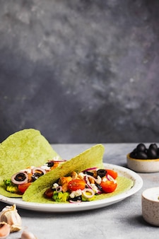 Takos avec guacamole, poulet frit, fromage cottage, tomate, oignon rouge, ail, olives en tortilla verte avec basilic et épinards. vue de dessus avec fond
