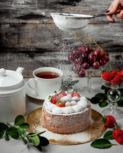 Tamis en poudre de femme sur le gâteau aux fruits