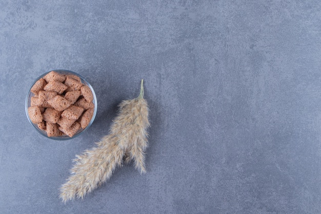 Tampons de maïs au chocolat dans un verre à côté de l'herbe de la pampa, sur la table bleue.