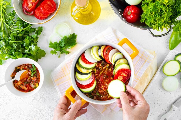 Étape 3 Différents légumes Une alimentation saine Ingrédients pour la cuisson Ratatouille de légumes sur fond blanc Mains dans le cadre Vue de dessus