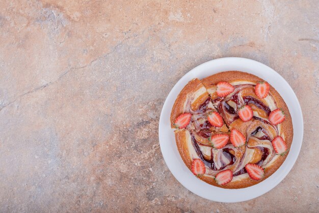 Tarte aux fraises au sirop rouge et fruits dans une assiette blanche.