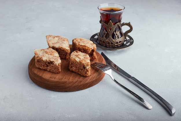 Tarte en tranches sur un plateau en bois avec un verre de thé sur une surface blanche.