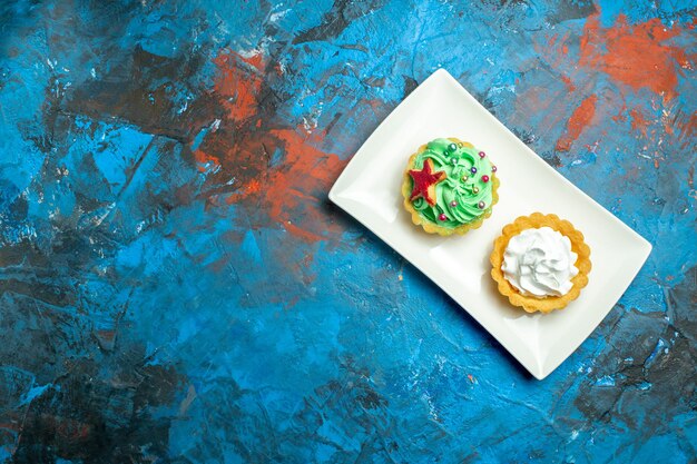 Tartelettes à la crème vue de dessus sur plaque rectangulaire blanche sur espace libre de surface rouge bleu