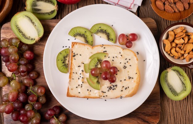 Tartinez le pain de confiture et placez-le avec le kiwi et les raisins sur une assiette blanche