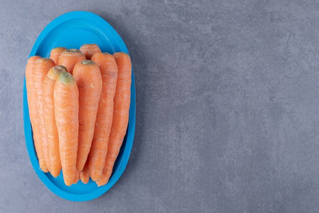 Un tas de carottes sur le plateau bleu , sur le fond de marbre.