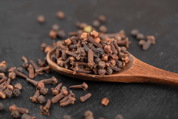 Tas de clous de girofle naturels séchés avec une cuillère en bois sur une surface noire.