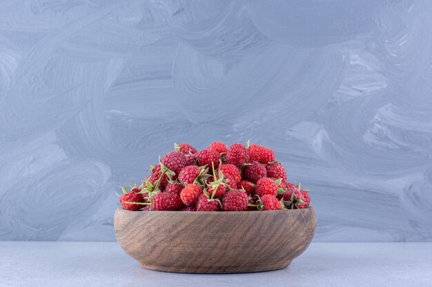 Tas de framboises délicieux dans un bol en bois sur fond de marbre. photo de haute qualité