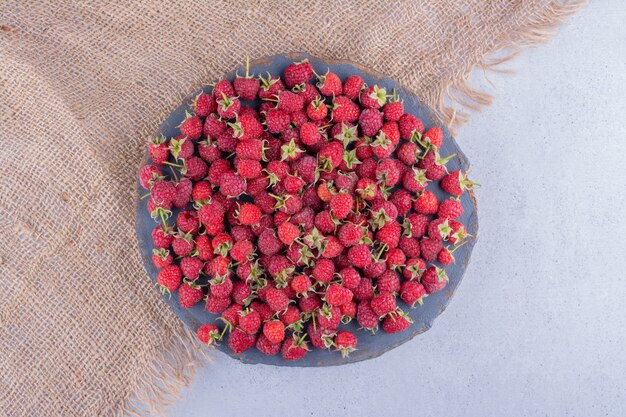 Tas de framboises sur une planche de bois sur fond de marbre.