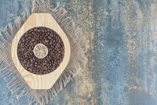 Tas de grains de café et tranche de citron sur plaque de bois.