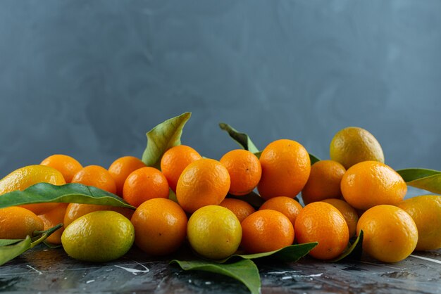 Tas de kumquats mûrs avec des feuilles vertes sur une surface en marbre.